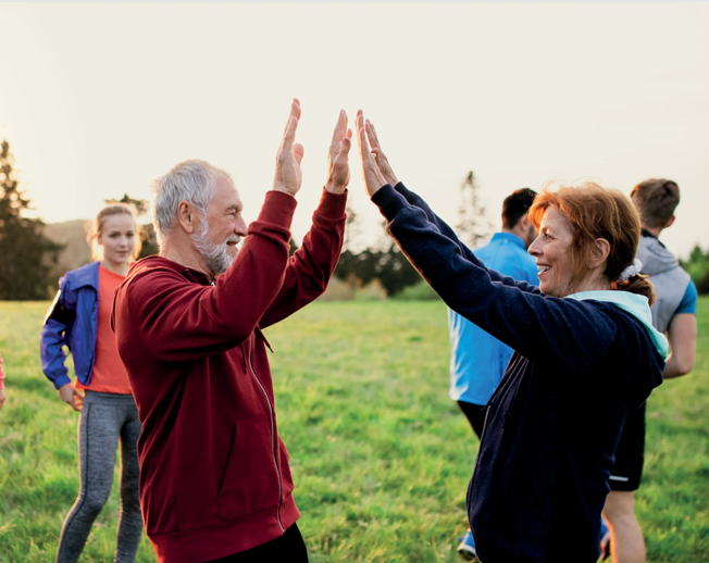 Auf dem Bild sieht man Menschen jeden Alters in Alltagskleidung Sport im Park machen und sich gemeinsam zu bewegen